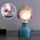 Orange and green resin desk lamp featuring a chic, minimalist design, illustrated with a playful, animated fictional character in a still life setting.