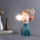 Artistic resin desk lamp featuring a chic, minimalist design in orange and green, illustrated with eye, eyelash, and jaw motifs, set against a wooden background.