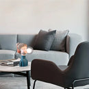 Chic minimalist design desk lamp in orange and green, displayed on a wooden table beside a couch with pillows in a comfortably styled living room setting.
