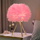 Pink and orange feather LED table lamp with dimmable lighting, styled in a vase on a table, surrounded by a floral textile design.