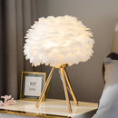 White Feather LED Table Lamp with dimmable lighting, featuring a floral design with petals, artfully placed in an interior setting near a window with curtains and a picture frame.