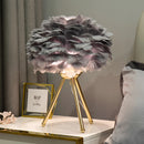 White feather LED table lamp on a table, surrounded by a vase, picture frame, and subtle floral elements in a stylishly decorated room.