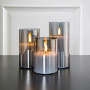 Three-piece flameless glass candle set featuring LED pillar candles in cylindrical holders, displayed with plant and flowerpot accents.