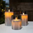 Three-piece flameless glass candle set with LED pillar candles, displayed with a remote control, on a table setting.