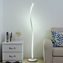Silver floor lamp with remote control featuring three light temperatures, set beside a grey dresser in a comfortably furnished room.
