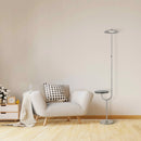 Wooden floor lamp with a built-in wireless charging station and rectangular table top shelf, placed next to a grey couch in a comfortable interior setting.