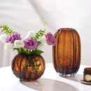 Purple artificial flower arrangement in a glass cactus-shaped vase on a table.