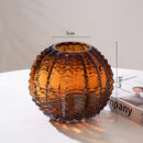 Small brown glass cactus vase designed to resemble a lantern, featuring artistic tints and shades with wood and metal accents, displayed in a circular light fixture setup.