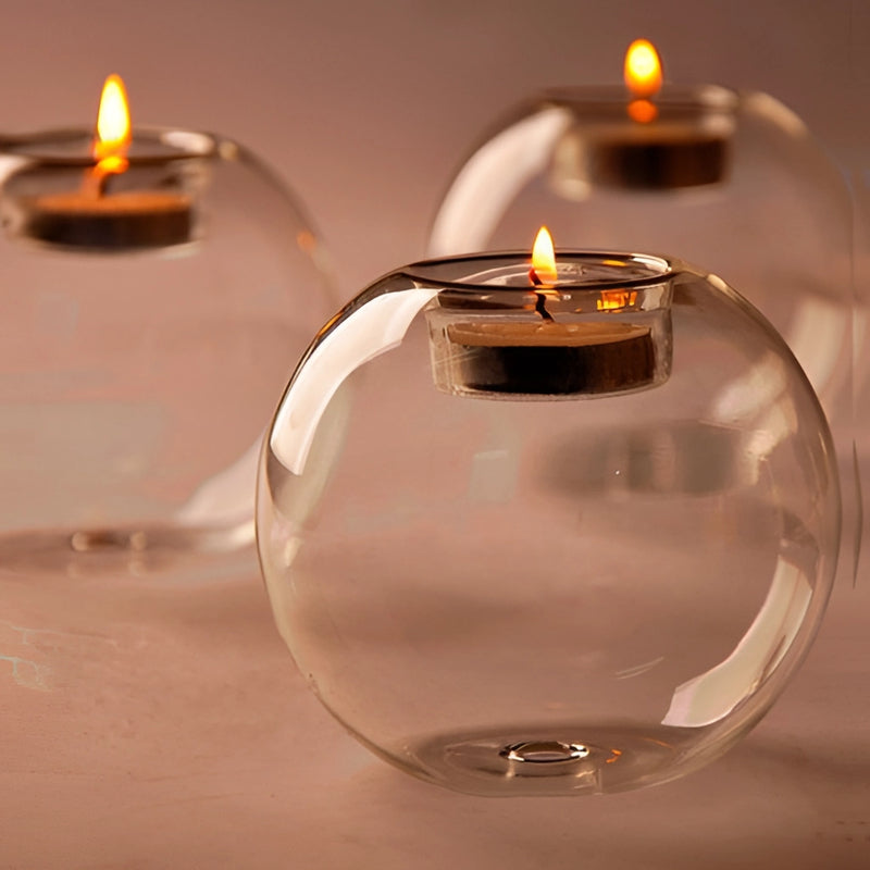 Glass candle holder designed for votives and tealights, featuring a transparent and fluid-like design that can be mistaken for drinkware or perfume.