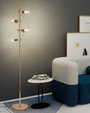 Gold diamond-patterned floor lamp with adjustable angles, positioned near a grey couch and rectangular shelving, enhancing a cozy and artistic interior space.