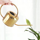 Gold stainless steel watering can surrounded by plants and flowers, featuring a sleek, metallic design.