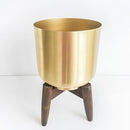 Golden iron plant stand featuring a cylindrical metal frame on a wooden base, with artistic details.