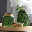 Green glass vase designed for hydroponic plants featuring a Nordic style, displayed with plants and surrounded by minimalistic dishware and textiles, enhancing a modern interior design.