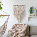 Handwoven Macrame Boho Wall Hanging Tapestry with geometric designs, displayed above a white couch in a room with wooden accents and natural branch decorations.