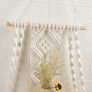 Handwoven beige and white macrame boho wall hanging tapestry featuring geometric patterns and creative arts, embellished with twigs and displayed on a wooden background.