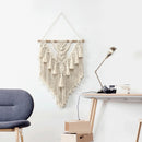 Handwoven Macrame Boho wall hanging tapestry featuring geometric art decor, displayed against a grey hardwood interior with shelving and a chair.
