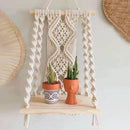 Handwoven Macrame Boho Wall Hanging Tapestry featuring geometric patterns, displayed on a wooden shelf with houseplants and decorative ornaments.