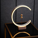 Interior lamp featuring a crescent-shaped glow, made of wood and metal with hardwood accents, showcasing a blend of rectangular and oval shapes with artistic tints and shades.