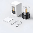 LED aromatherapy diffuser with a cylindrical metal design, featuring a candle light effect and displayed on shelving with various electronic and audio equipment accessories.