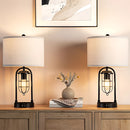 White LED desk lamp with dual bulb design, featuring USB ports, placed on a wooden countertop near a plant inside a well-lit room with cabinetry and drawers.