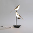 LED desk lamp featuring a postmodern design with a galvanized golden bird perched on a twig, crafted from metal and wood, showcasing artful balance and intricate details.