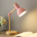 Scandinavian minimalist design LED desk lamp in Rosa, featuring a lampshade with three color settings and a switch, displayed on a wooden table next to a vase with flowers and plants for a comfortable ambiance.