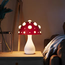 Warm white LED mushroom table lamp with a lampshade, displayed on a wooden table, enhancing the room's interior design with subtle patterns and lighting.