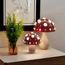 Warm white LED mushroom table lamp displayed on a wooden table, surrounded by houseplants and flowerpots, enhancing the cozy interior design.