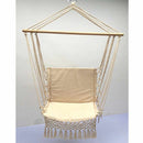 Macramé hammock swing made of wood and metal, styled with decorative accessories like a basket, lamp, and bag, displayed in a shaded garden setting.