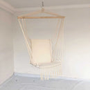 Macramé hammock swing made of natural materials, suspended from a ceiling with a light fixture visible above and glass elements in the background.