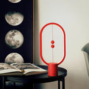 Magnetic Balance Table Lamp with LED lighting, featuring a unique rectangular design that resembles a moon, placed on a table surrounded by books, enhancing an artistic interior setting.