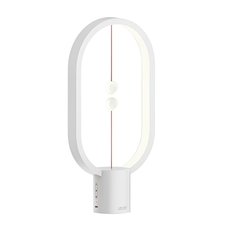 White Magnetic Balance Table Lamp with LED Lighting featuring a modern design with peripheral cables and a plant in the background.