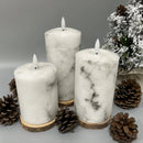 Set of three white marble LED flameless candles in cylindrical shapes, displayed with pine twigs and candle holders, suitable for events.
