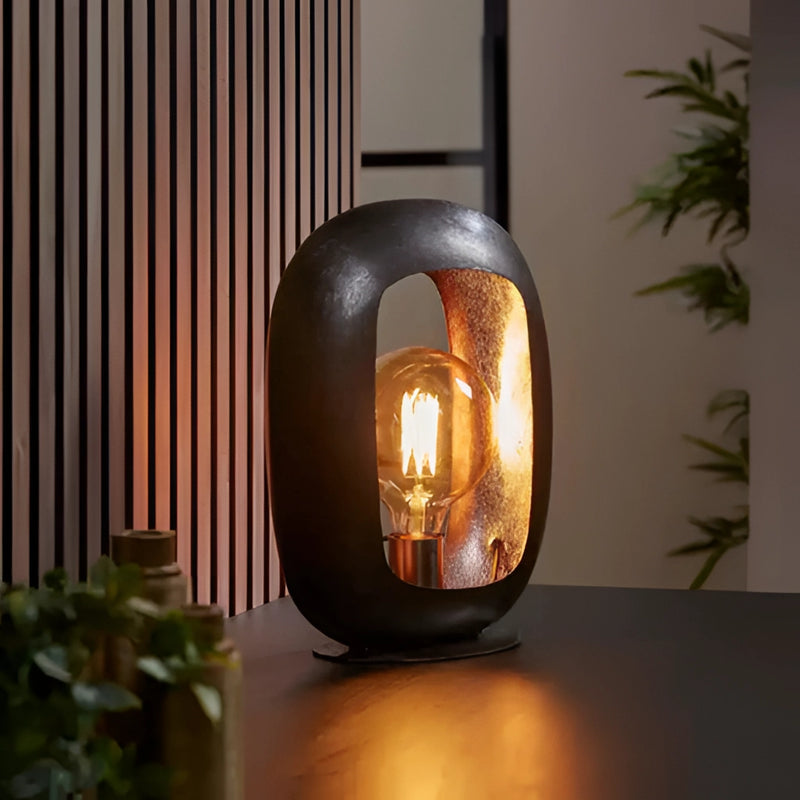 Vintage style metal table lamp with amber-colored glass, set on a wooden base, featuring intricate artistic details and emitting a warm, soft glow.