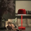Adjustable metal table lamp with brightness control, Pulse Flare model, displayed on a table next to a houseplant in a flowerpot, in a well-lit room setting.