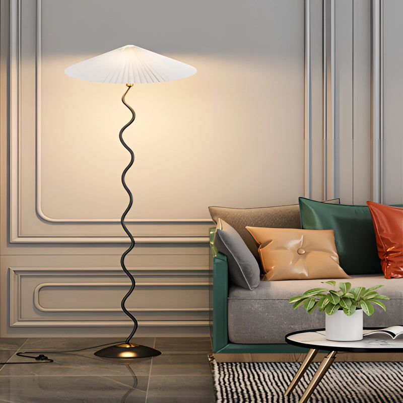 White and grey curved pleated floor lamp with a metal base, positioned next to a couch in a stylish interior setting.