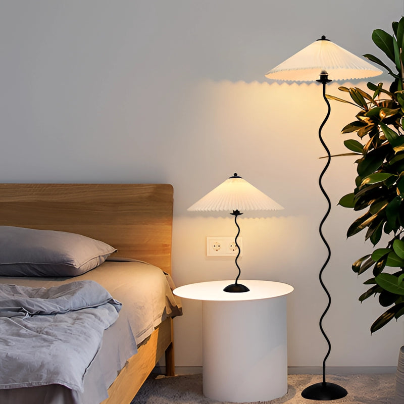 Curved pleated floor lamp with a metal base and textile shade, placed in an interior setting, enhancing the room's comfort and design.