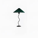 Teal table lamp with a curved, pleated metal textile shade, accompanied by a plant, providing a balanced and stylish light fixture.