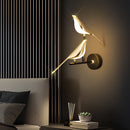 A modern rotatable wall sconce with a 360-degree lampshade in gold, positioned near a black couch and a wooden table, casting a warm yellow light in a comfortably styled room with artistic decor.