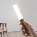 Rechargeable LED night light with wooden design featuring motion sensor technology, displayed with a hand gesture activating the light, set on a hardwood surface.
