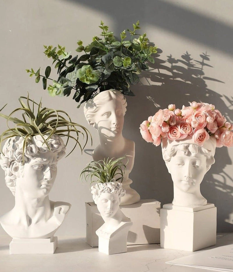 Resin vase designed as a neoclassical Greek head, filled with houseplants and flowers, showcasing detailed botanical and creative arts influences in an interior setting.