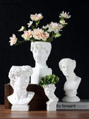 Neoclassical Greek head-shaped white resin vase with artificial flowers and plant arrangement, showcasing detailed sculpture and art elements.
