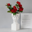 Resin vase designed as a Neoclassical Greek head, filled with vibrant hybrid tea roses and other plants.