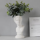 Neoclassical Greek head resin vase styled as a sculpture containing a lush houseplant, artistically blending botany with art.