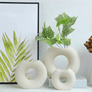Nordic style ceramic donut vase featuring a modern circular design, displayed on a shelf with a houseplant inside, enhancing an office or living room setting.