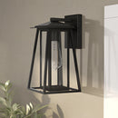 Black steel outdoor wall lantern sconce with glass panels, IP44 waterproof, mounted on a wooden shelf surrounded by plants.