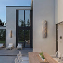 Outdoor wall light featuring IP65 waterproof rating with a premium resin faux rock finish, displayed on a building surrounded by plants.