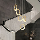 Modern Dante pendant lamp featuring a rectangular black and gold chandelier against a wooden wall with various light shades.