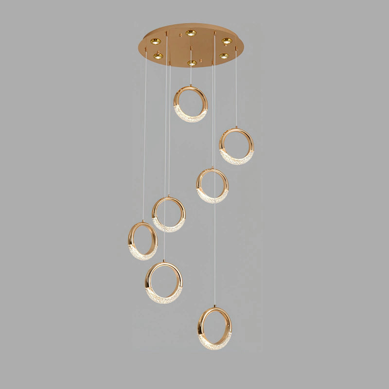 Gold Pendant Lamp Dante featuring seven circular heads with cool light, suspended from the ceiling, showcasing a modern chandelier design with a pattern of amber-colored metal elements.