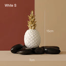 Golden resin ornament shaped like a pineapple, displayed in a white flowerpot, featuring natural wood elements.